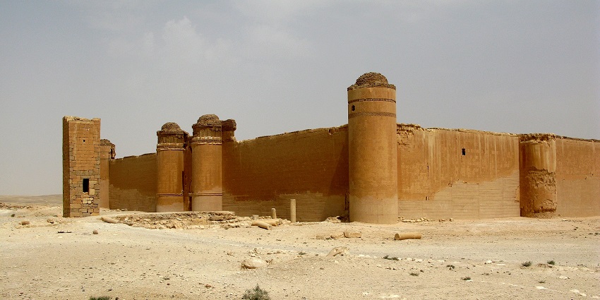 Qasr al-Hayr al-Sharqi from outside with broken walls, watch towers and sandy ground