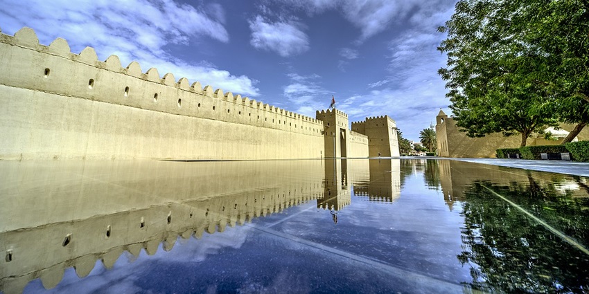 Reflections of Qasr al Muwaiji Fort with architecture, distant flag on top of the fort.
