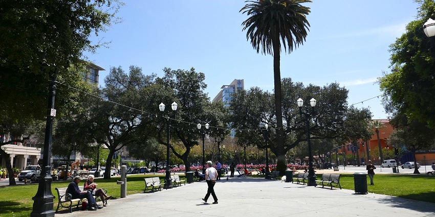 A view of Plaza de César Chávez with people on the street & sitting on the benches.