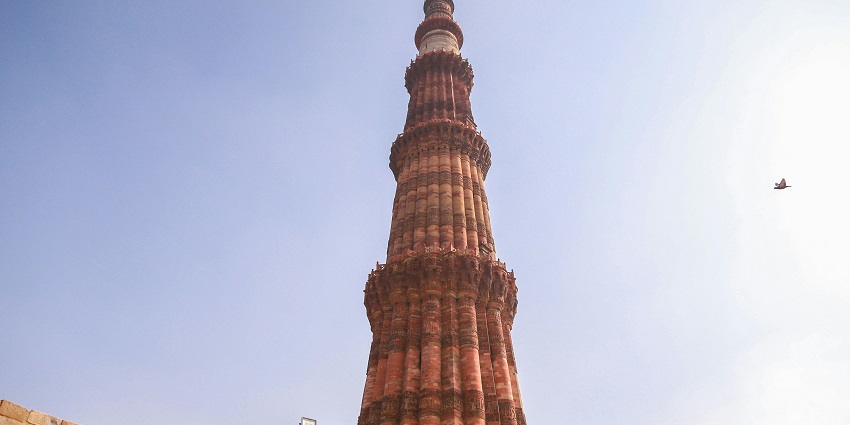 An image of Qutub Minar with detailed old Islamic architecture and stone walls.