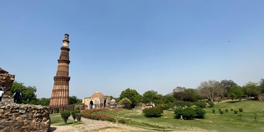 Qutab Minar complex with old architecture of the tall Qutab Minar, distant old buildings and a garden