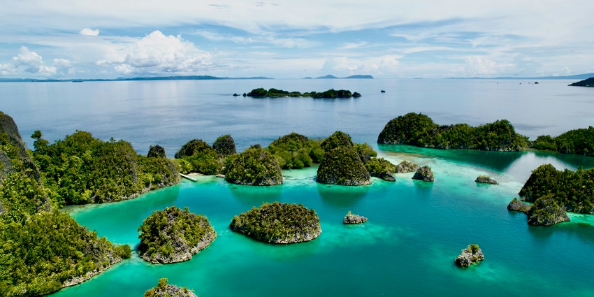 Panoramic view of turquoise waters and lush islets under a bright, cloud-filled sky, one of the best places to visit in Indonesia in December.