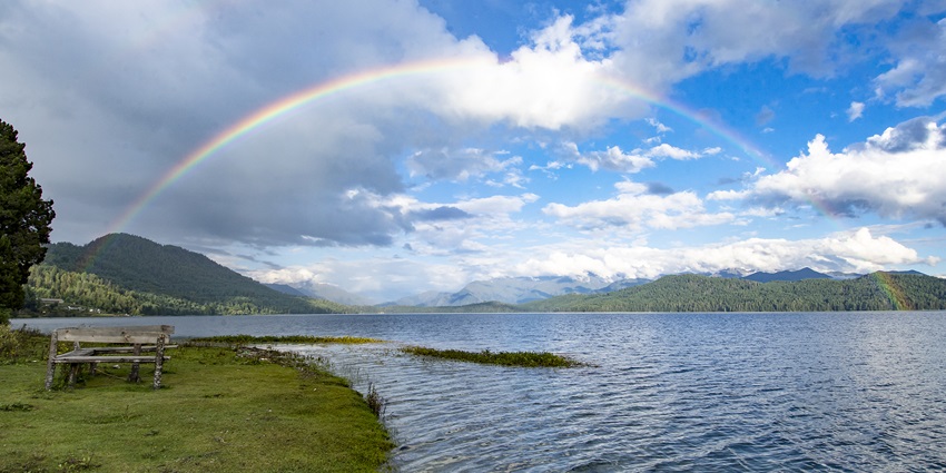 A rainbow arching over the serene blue waters of the majestic Rara Lake in Nepal.