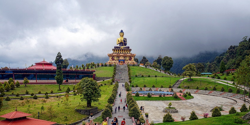 A Buddha statue towers above a hilltop park bordered by pine trees, one of the top places to visit in Sikkim in October.