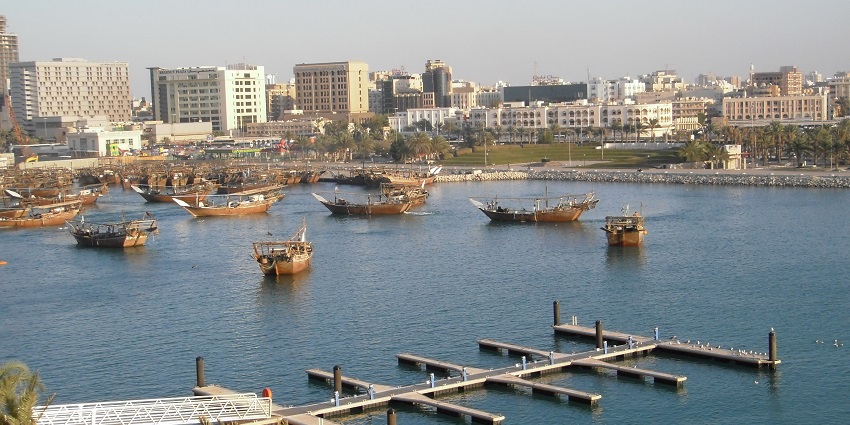 A scenic view of Reef Island with modern buildings, palm trees, and calm blue waters under a clear sky.