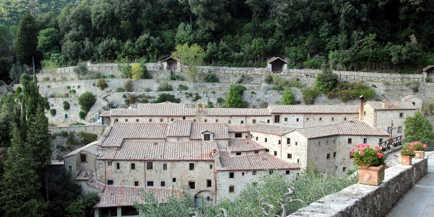 Image of a historic stone monastery nestled in the green hills of Cortona, Italy.