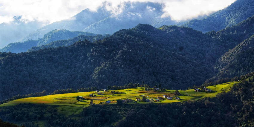 Village in Bhutan with distant small houses, farms, green trees and surrounded by mountains.