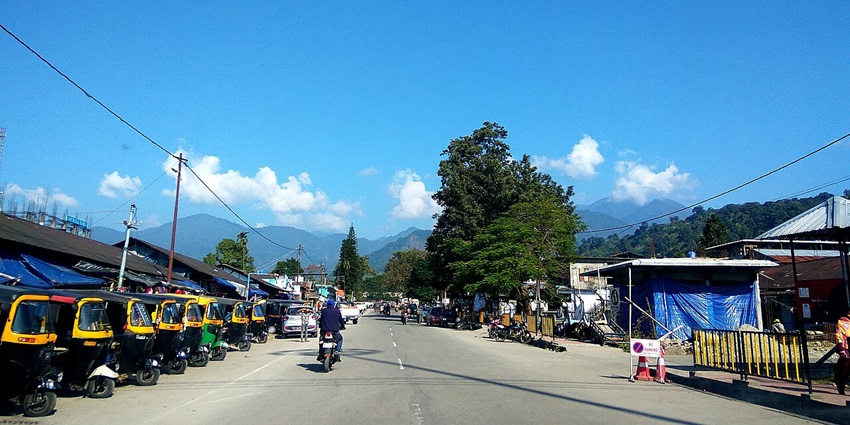 Welcome gate to Roing with police barricades, vehicles, tall green trees and mountains