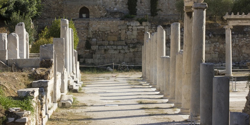 Row of ancient stone columns in front of a weathered stone wall with scattered ruins.