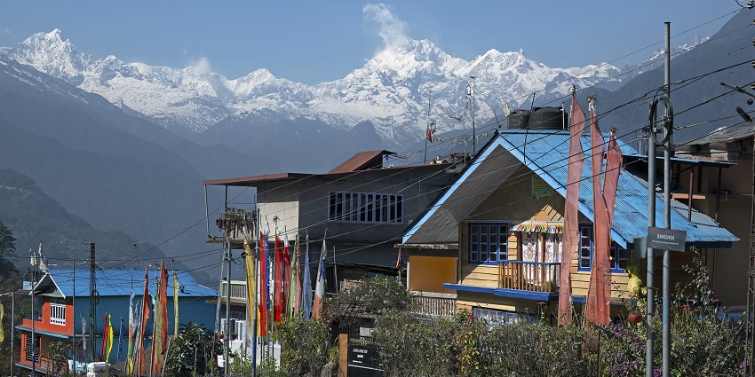 A traditional Rorathang village with houses and forested hills below a snow-covered mountain, one of the top places to visit in Gangtok in June.