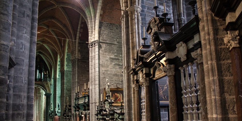 Interior of Saint Bavo's Cathedral with vaulted ceilings and colourful glass windows.