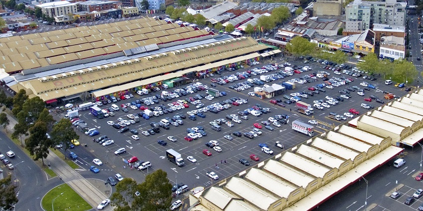 Aerial view of a large market complex surrounded by a busy parking lot and city buildings.