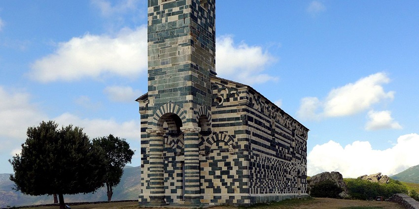 San Michele de Murato with green and white architectural build, green trees in the back.