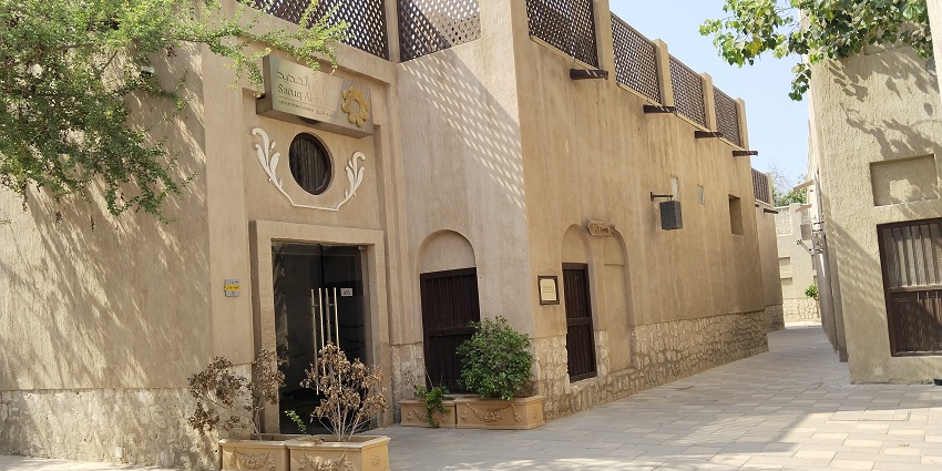 Traditional beige buildings with wooden doors and lattice work along a quiet paved alley, one of the best historical places in Dubai.