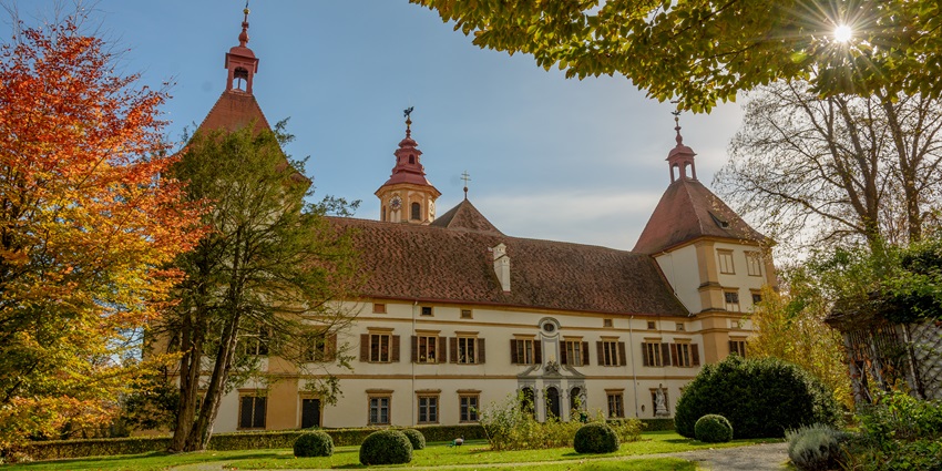 Schloss Eggenberg, one of the grand historical places in Austria, is surrounded by green lawns and a clear sky on a sunny day.