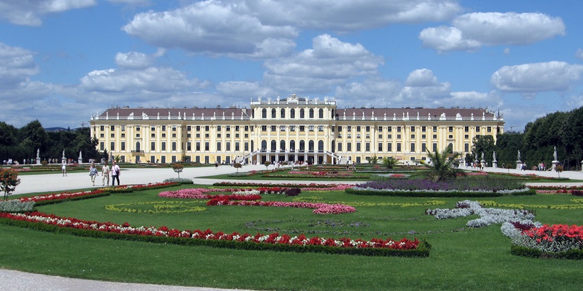 Schönbrunn Palace in Vienna with its grand yellow facade, gardens, and clear blue sky on a sunny day.