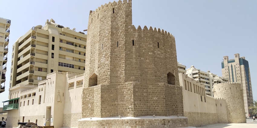 Sharjah Fort with traditional architecture, old cannons and a man standing on the entrance, one of the top monuments in Sharjah.