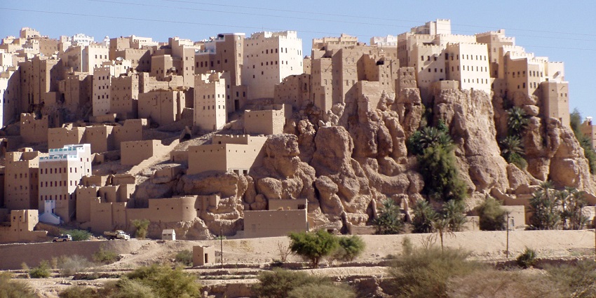 Tall mudbrick skyscraper buildings are tightly clustered in a historic desert cityscape, one of the historical places in Yemen.