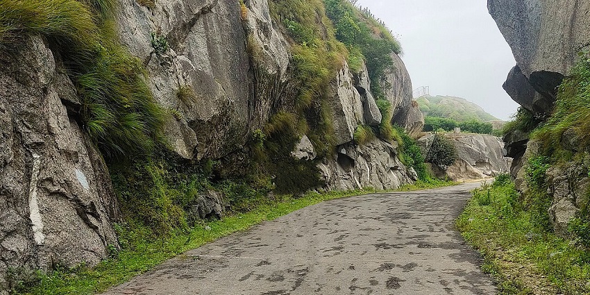 Trekking trail to Guru Shikhar with green grass on both sides of the trail and big rocks.