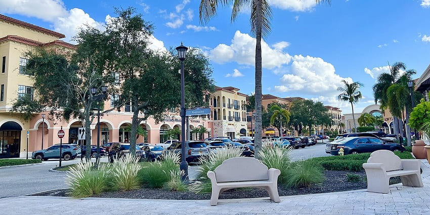 Outdoor mall with palm trees, fountains, and people walking by storefronts in Coconut Point.