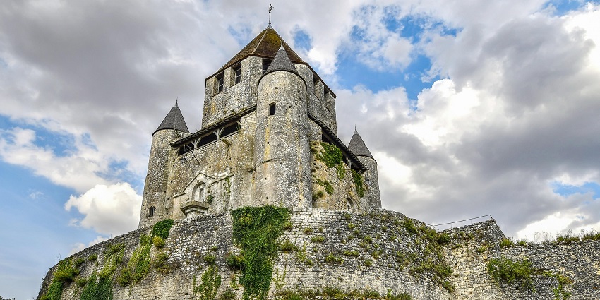 Stone castle on a hill with conical towers and ivy-covered walls, resembling the historic architecture of Sira Fortress.
