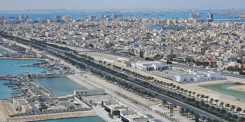 Aerial view of Sitra Island, showing coastline, buildings, and greenery under a clear sky in Bahrain.