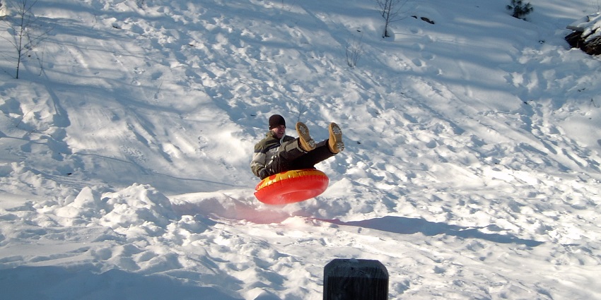 A woman enjoying snow tubing, sliding down a snowy hill with joy, surrounded by white snow and winter scenery.