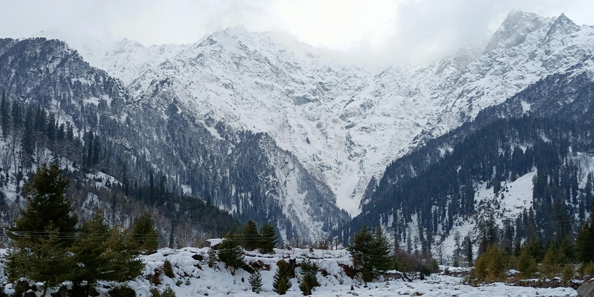 A snow-covered town nestles in a valley surrounded by snow-capped mountains under a clear blue sky.