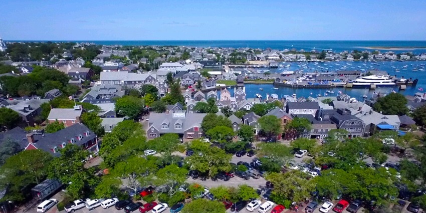Aerial view of Nantucket town with coastal homes, docks, and surrounding blue waters.