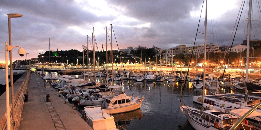 Scenic view of Fort Madison Marina with anchored boats, calm waters, and coastal buildings set against a hilly backdrop.
