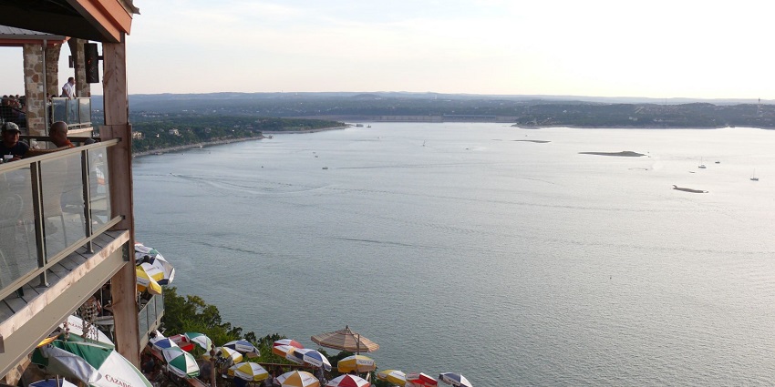 Peaceful view of Lake Travis with boats, calm blue water, and green shoreline under clear skies.