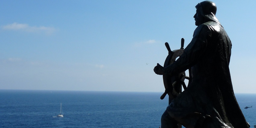 Bronze statue of Prince Albert I of Monaco facing the vast blue sea while holding the wheel