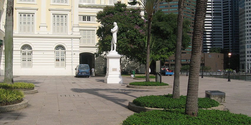 A white statue of Sir Stamford Raffles with arms crossed, standing on a pedestal.