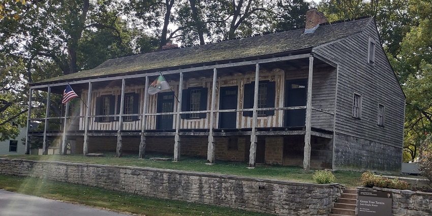 Green tree traven in Ste. Genevieve National Historical Park with an old building and two flags