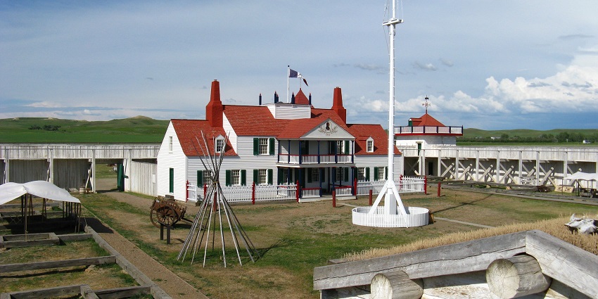 Historic wooden fort structure with enclosed courtyard, gates, and open grassland around.