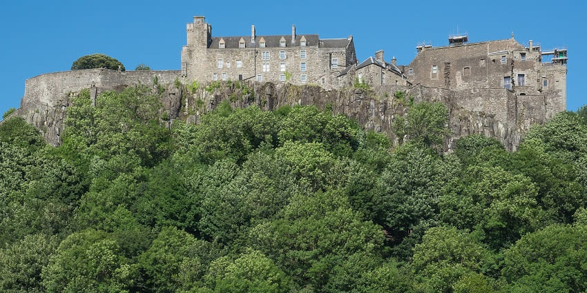 Stirling Castle from a distance with old architecture, multiple glass windows and green trees.