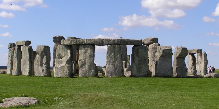 Stonehenge in Wiltshire with tall pillars of natural stones, green grass plain and people visiting