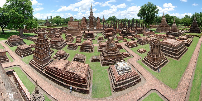 Ancient ruins and temples at Sukhothai Historical Park, surrounded by greenery under a clear blue sky, one of the top monuments in Thailand.