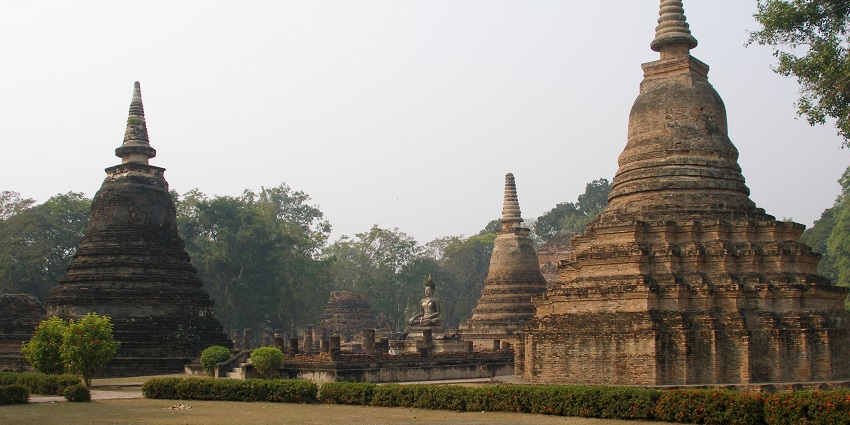 Buddhist temples and stupas in Sukhothai with a distant statue of Buddha and old architecture, one of the iconic places to visit in Thailand in January.