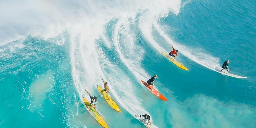 An image of surfers riding waves near the beach with bright sky and sparkling ocean water.
