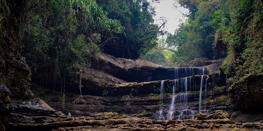 Waterfall in Meghalaya with multiple water streams falling, uneven rocks and greenery.