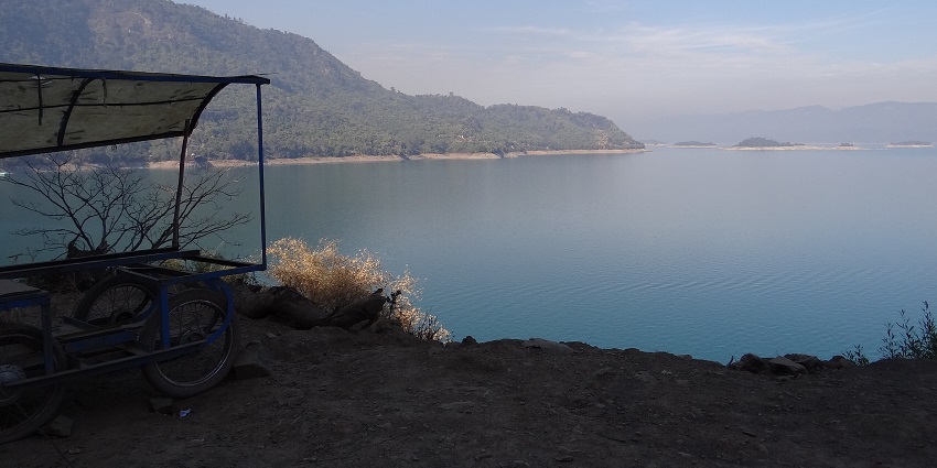 Fish sanctuary with a blue clear water body, distant sticks in the water and green hills.