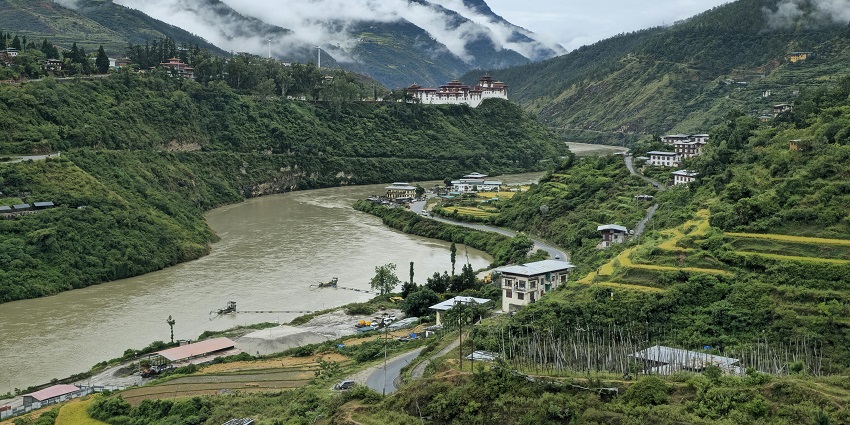 Village in Bhutan with a greenish water body of a river flowing, distant buildings and houses.