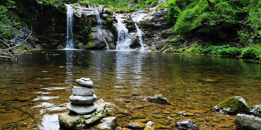 Taman Beji Griya Waterfall with water flowing into a lake and surrounded by lush greenery.