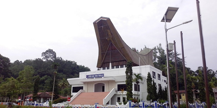 Modern building with traditional-style roof, surrounded by flowers and lush greenery.