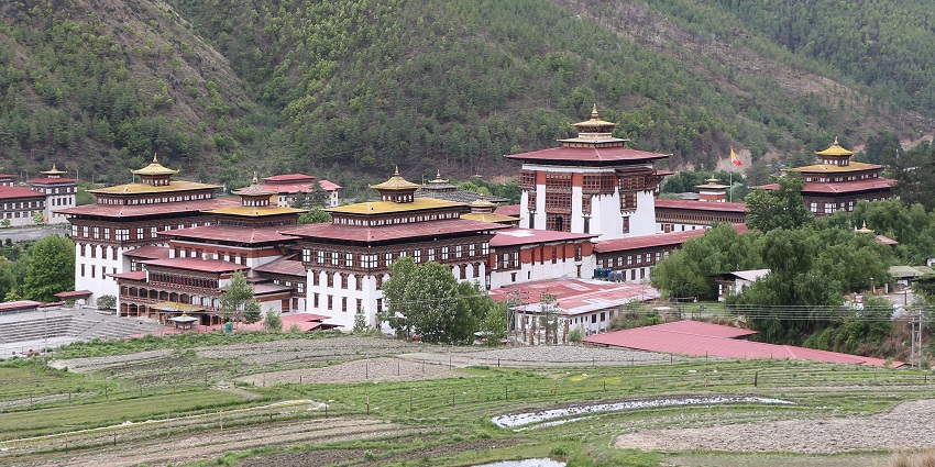 Elegant dzong with whitewashed walls and red-tiered roofs, set in a manicured green lawn under soft evening light.