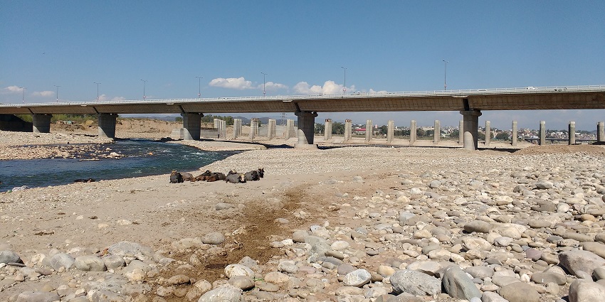 Stony surface along the Jammu Tawi riverbank with a bridge structure in the background