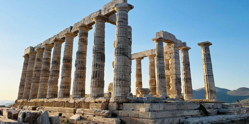 Ancient Corinthian-style stone columns stand tall against a clear sky and distant hills, one of the best historical Places in Athens Greece