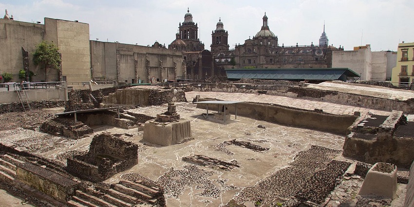 Ruins of Templo Mayor with broken stairs, walls, writings on the wall and vibrant buildings