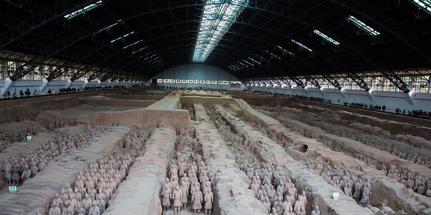 Terracotta army with multiple terracotta statues, lights on the ceiling and people visiting